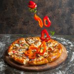 Side view pizza with slices of bell pepper and pizza slices and flour in board cookware on stone background